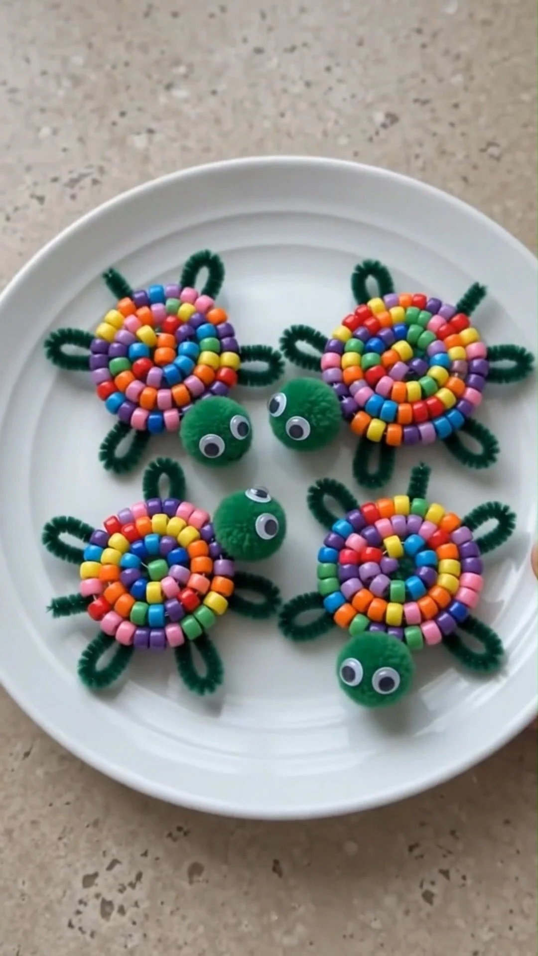 Bunte Ponyperlen, dunkelgrüne Pfeifenreiniger, Pompons und Wackelaugen ergeben niedliche kleine Schildkröten, die perfekt für kreatives Spielen sind.